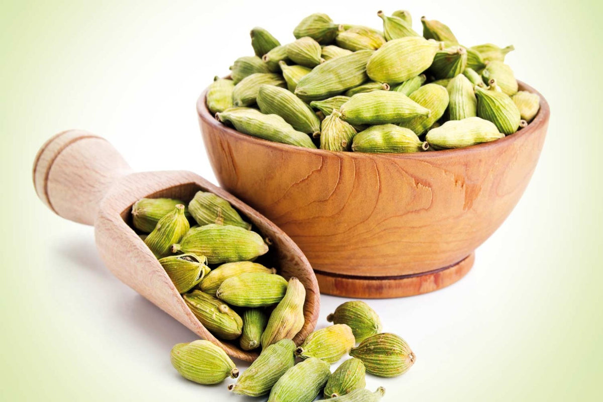 Green cardamom pods in a wooden bowl and scoop
